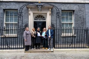 A group of three parents and OPFS representatives stand outside the black door of 10 Downing Street, holding a report after delivering the open letter.